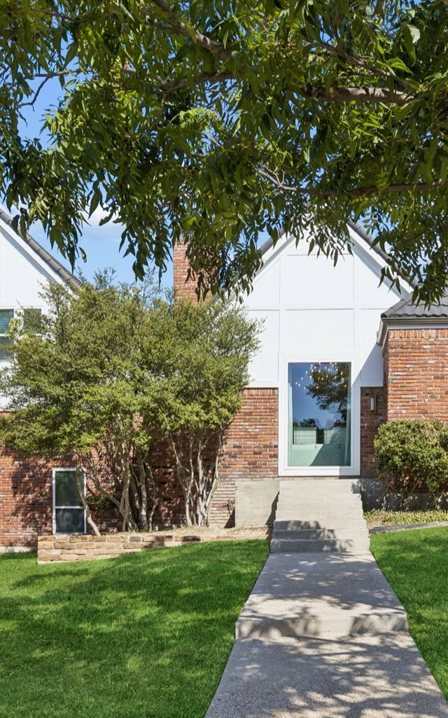 White and red-brick two-story cottage with a front lawn and a walk to the door.